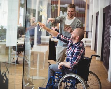 Das Bild zeigt einen Mann im Rollstuhl in einer Besprechung im Job.