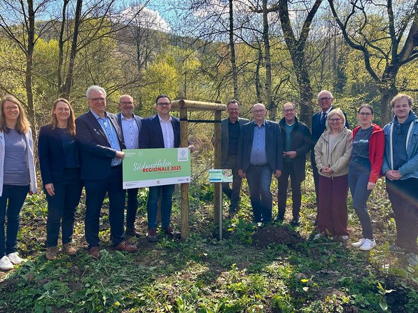 Bürgermeister Michael Joithe (5. v. l.) betonierte gemeinsam mit den Bürgermeistern der Partnerkommunen sowie mit Unterstützung durch die Südwestfalen Agentur GmbH und den Regionalmanagerinnen und -managern der drei LEADER-Regionen, das letzte Hinweisschild zur 'Essbaren Lenneschiene'.