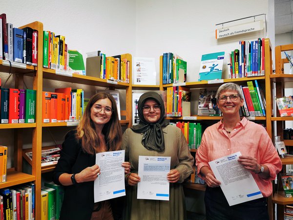 Stellten die Ausstellung „Gute-Laune-Geschichten“ in der Stadtbücherei Iserlohn vor (v.l.n.r.): Vasilisa Sterzer von der Migrationsberatung für erwachsene Zugewanderte (MBE) der Diakonie Mark-Ruhr, Selma Kuruoglu von der Migrationsberatung für erwachsene Zugewanderte (MBE) der AWO Hagen-Märkischer Kreis und Gudrun Völcker, Leiterin der Stadtbücherei Iserlohn.