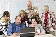 Das Bild zeigt eine Gruppe älterer Menschen an einem PC
