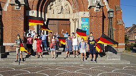 Das Bild zeigt Einwohner*innen der Stadt Laventie, die winkend und mit Deutschlandfahnen die Freundinnen und Freunde in Sümmern grüßen. 