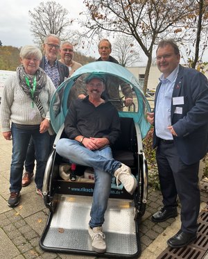 5 Personen stehen um einen Anhänger einer Fahrradrikscha, Doc Esser sitzt in diesem Anhänger