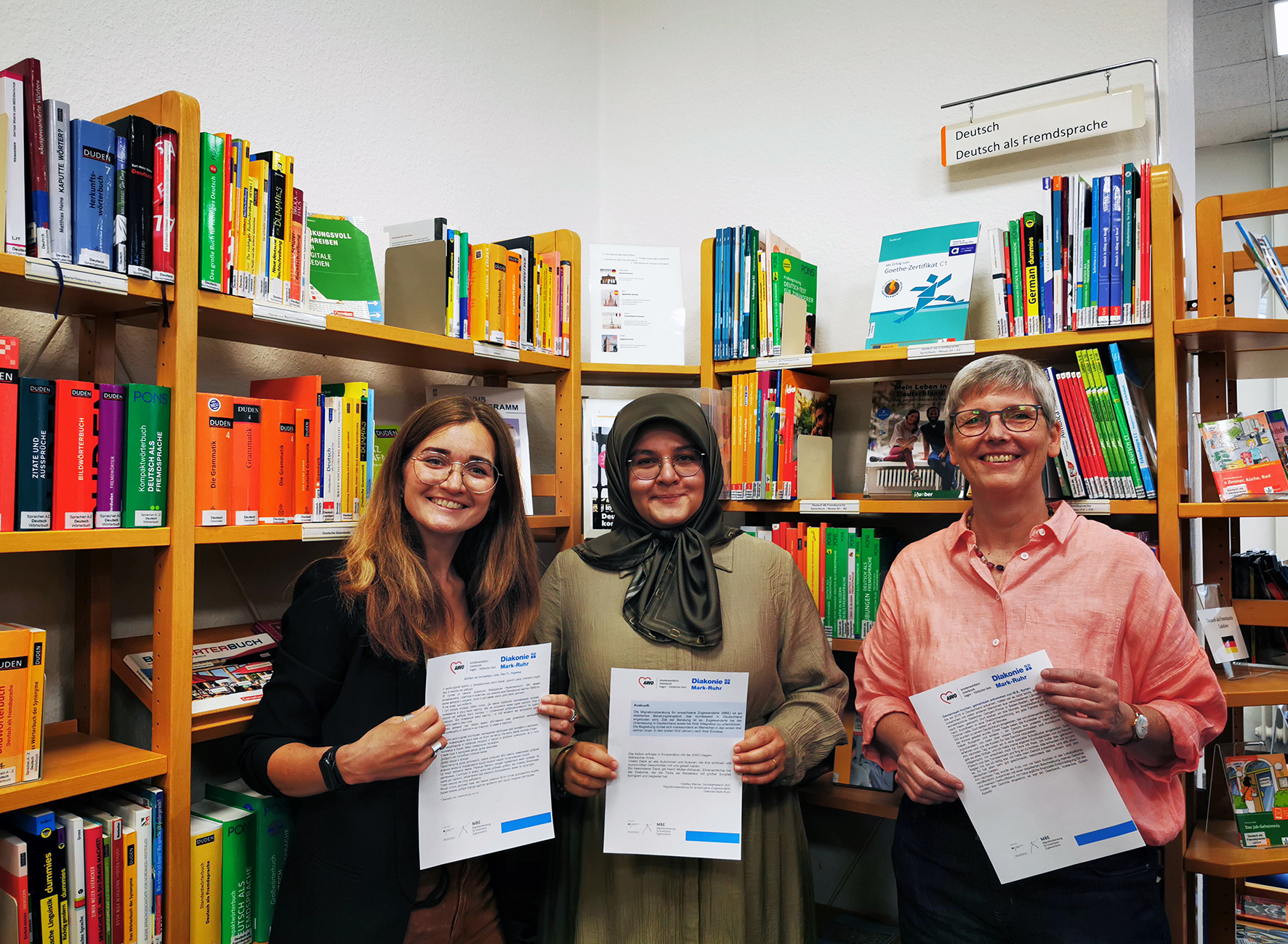 Stellten die Ausstellung „Gute-Laune-Geschichten“ in der Stadtbücherei Iserlohn vor (v.l.n.r.): Vasilisa Sterzer von der Migrationsberatung für erwachsene Zugewanderte (MBE) der Diakonie Mark-Ruhr, Selma Kuruoglu von der Migrationsberatung für erwachsene Zugewanderte (MBE) der AWO Hagen-Märkischer Kreis und Gudrun Völcker, Leiterin der Stadtbücherei Iserlohn.